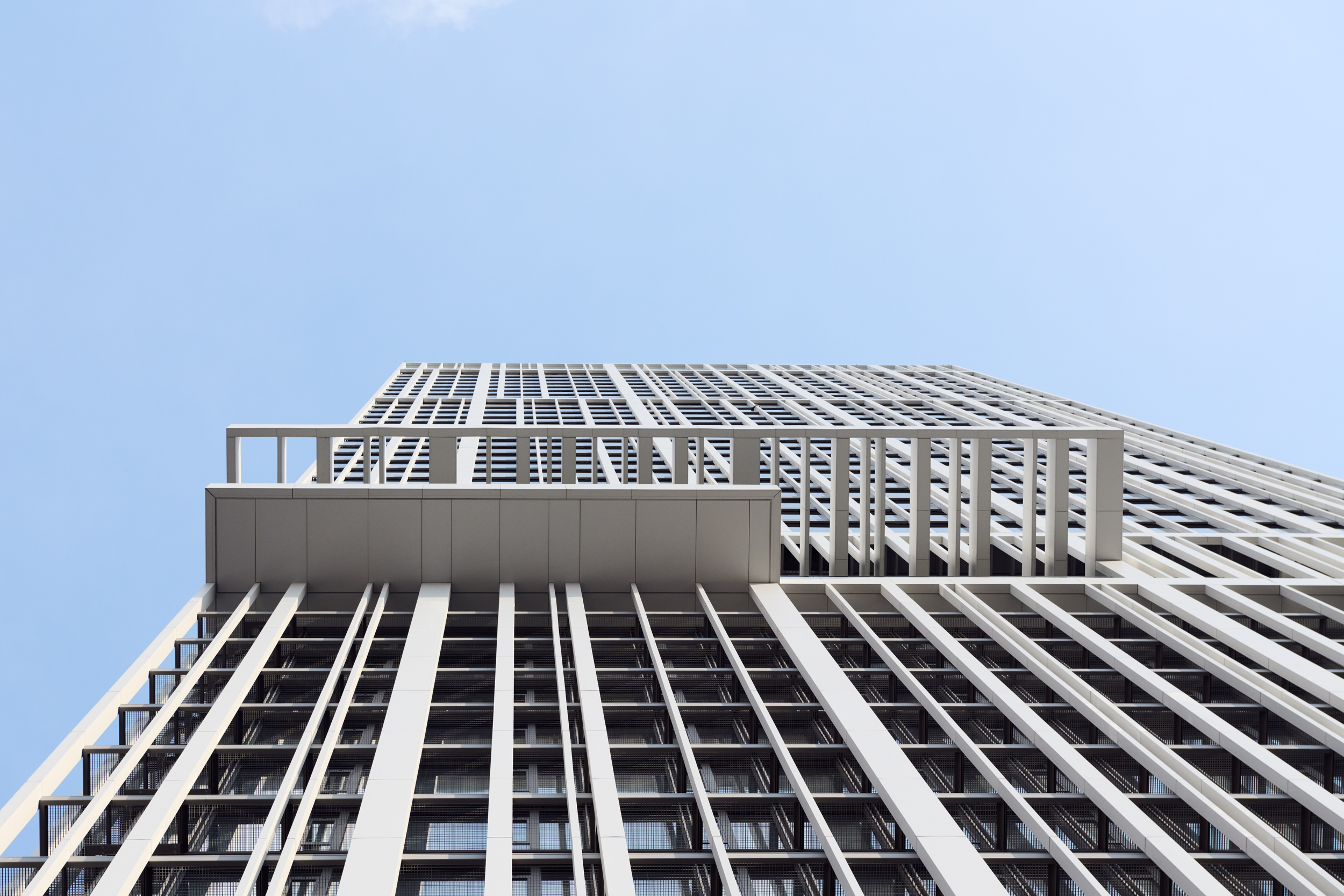 Low-angle view of a modern high-rise building with white vertical slats and a glass facade against a clear blue sky.