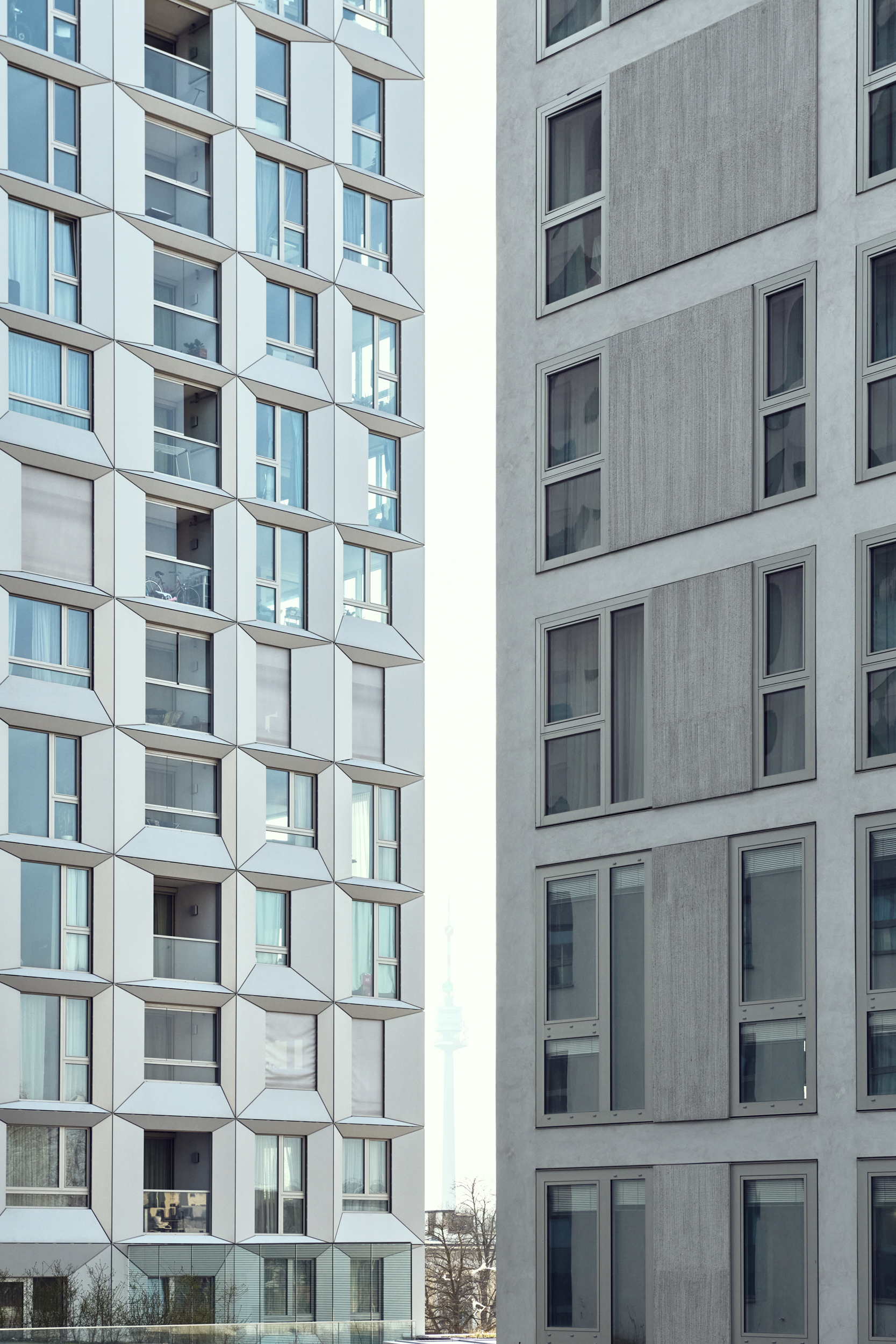 Two modern high-rise apartment buildings face each other with a narrow gap, showing a patterned facade of windows and balconies.