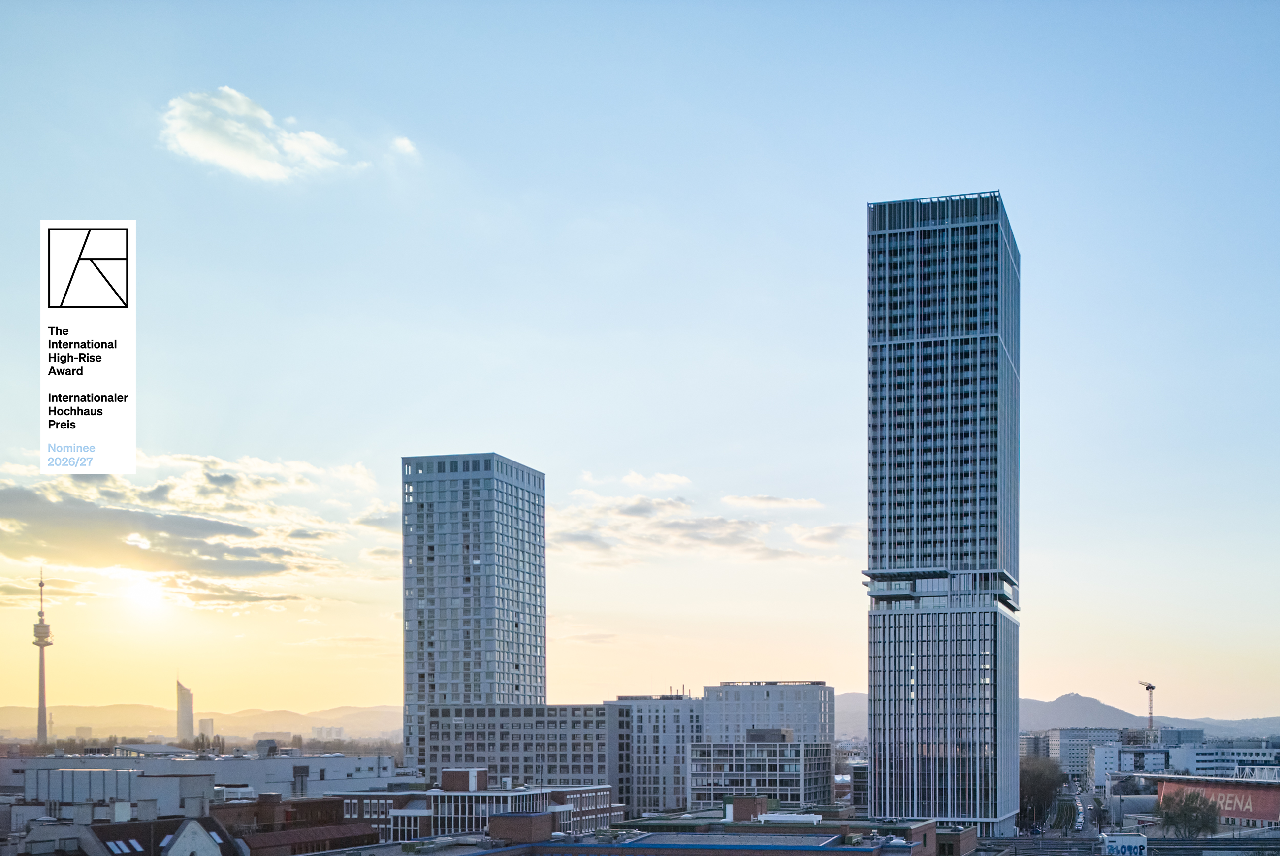 Sunset skyline with a tall glass-clad skyscraper on the right and a shorter rectangular high-rise to its left; a plaque on the left foreground.