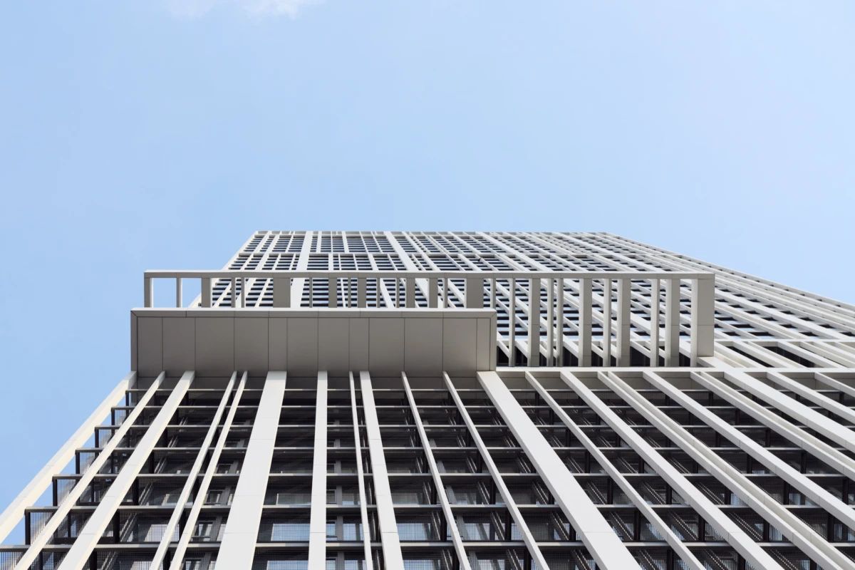 Low-angle view of a modern high-rise building with white vertical slats and a glass facade against a clear blue sky.