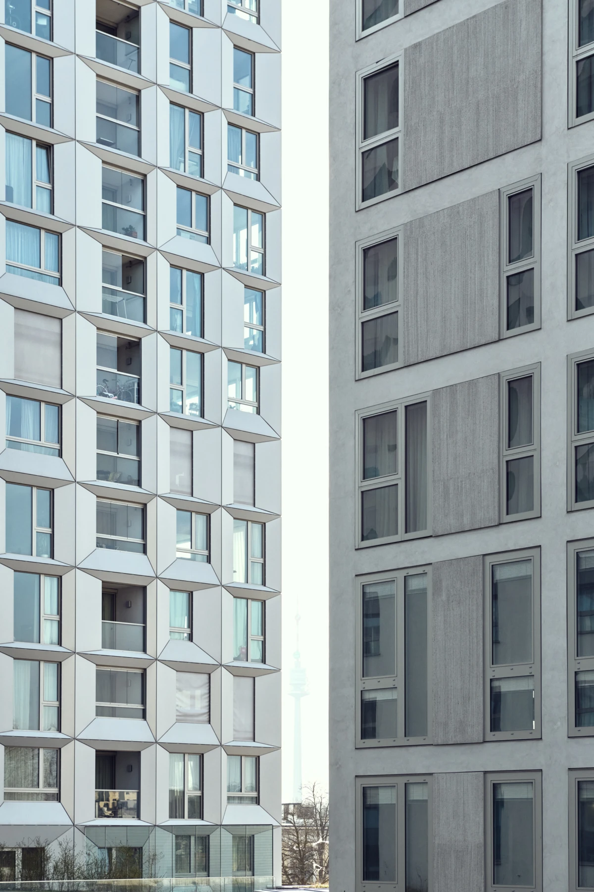 Two modern high-rise apartment buildings face each other with a narrow gap, showing a patterned facade of windows and balconies.