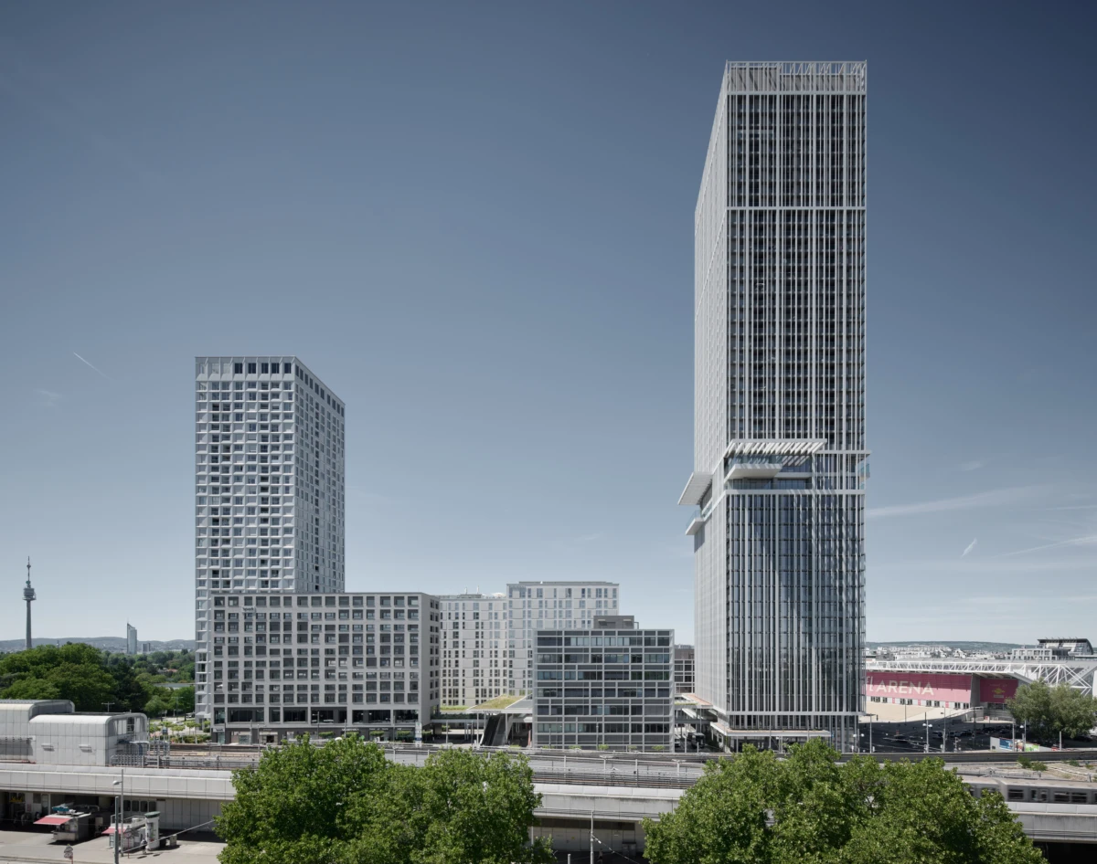 Cityscape with a tall slender skyscraper and a shorter glass-high-rise surrounded by mid-rise buildings and an elevated roadway in the foreground.