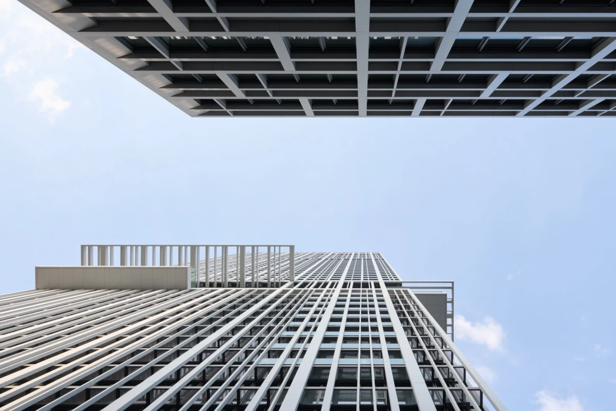 Two modern glass-clad skyscrapers rise toward a blue sky, viewed from street level.