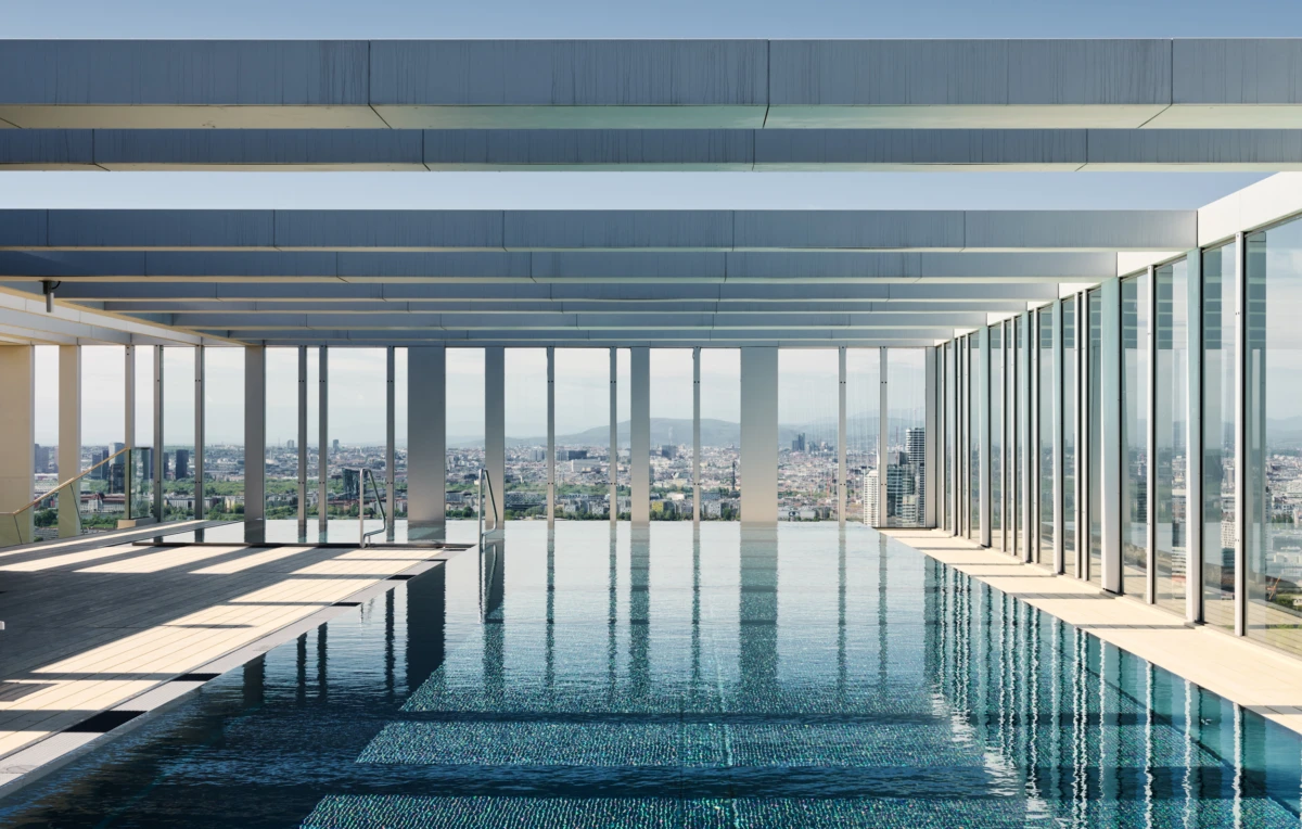 Infinity pool on a rooftop terrace with glass walls, calm water reflecting city skyline.