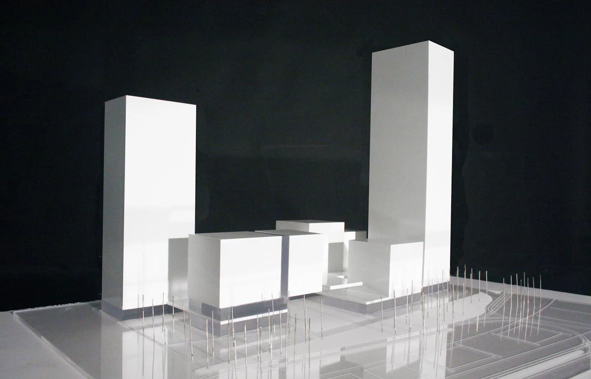 White architectural model of a modern complex with two tall towers and connected volumes on a clear base.