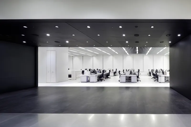 Open-plan office with rows of desks and chairs; employees work at computers in a bright white, modern workspace.