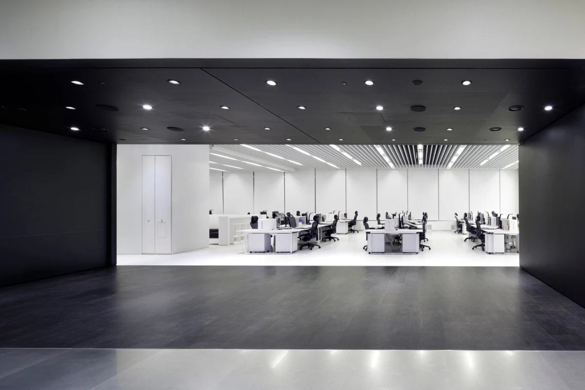 Open-plan office with rows of desks and chairs; employees work at computers in a bright white, modern workspace.