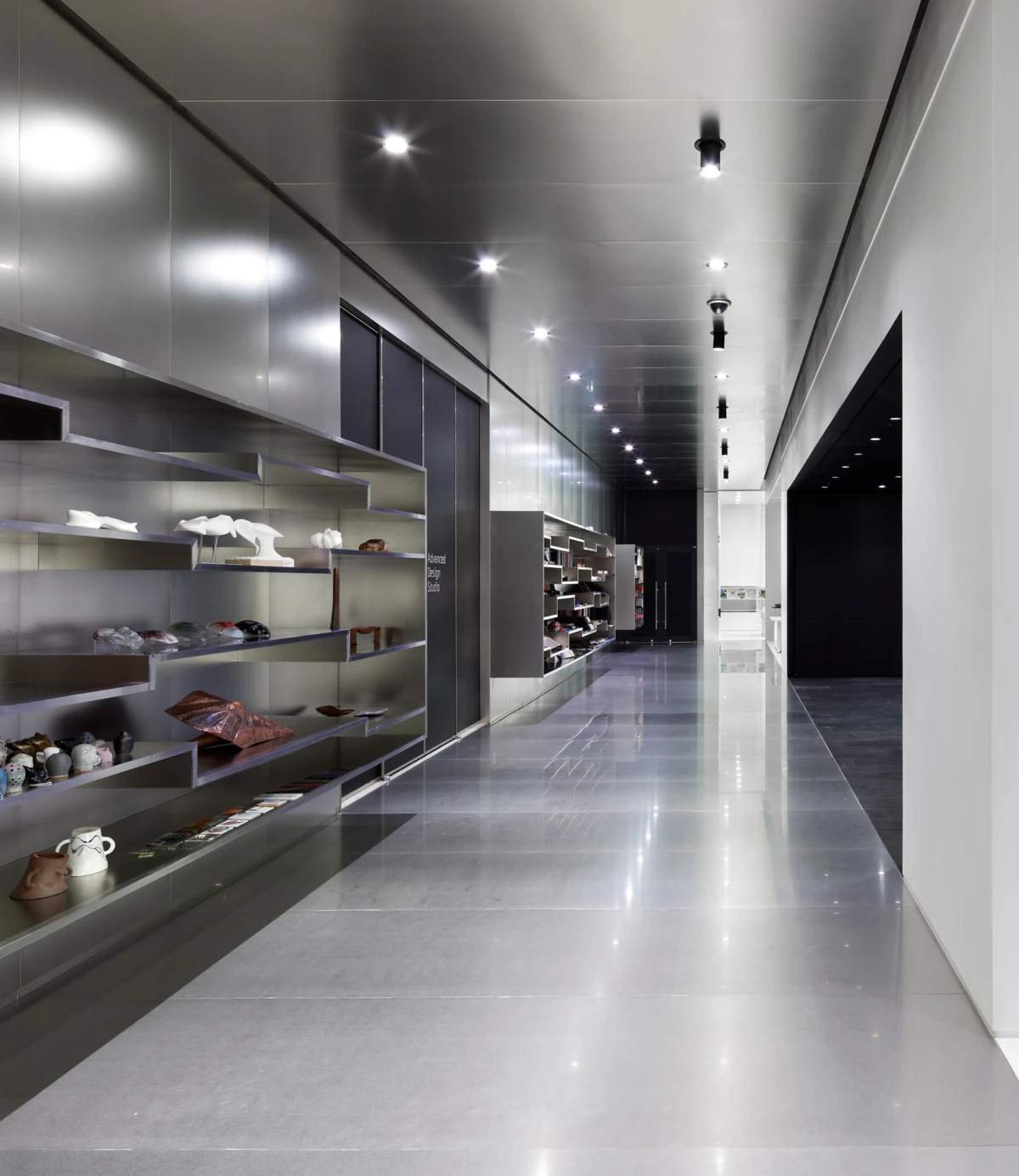 Long showroom hallway lined with metallic display shelves displaying shoes and handbags.