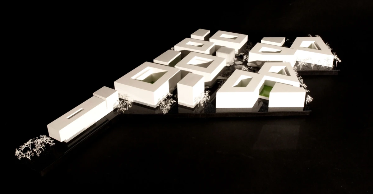 Scale model of a modern building complex with white blocky structures and inner courtyards on a black base, with trees along the edge