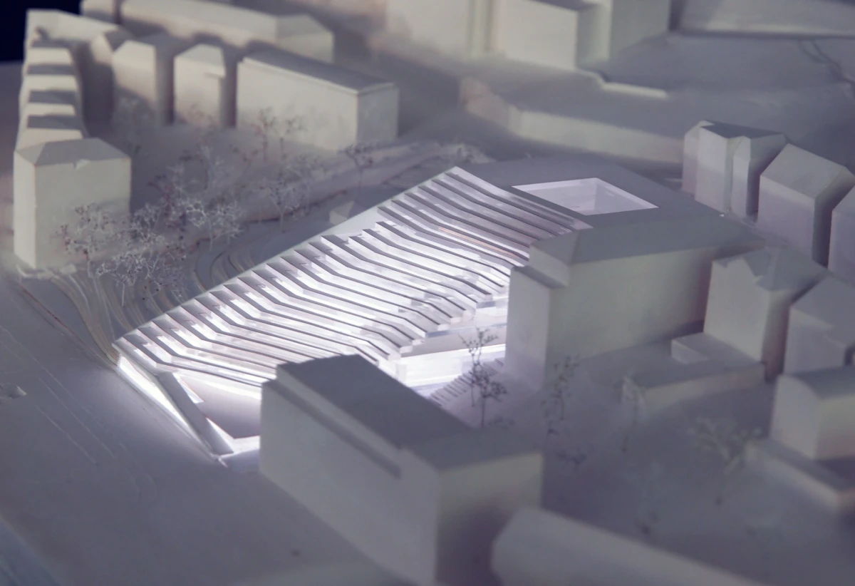 White architectural model of a curved, tiered amphitheater within an urban block.