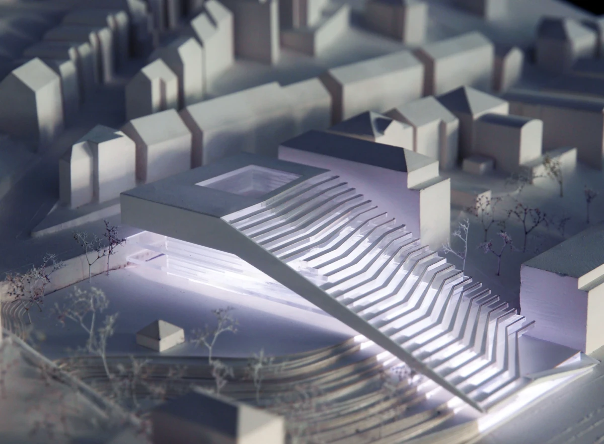 White architectural model of a modern building with a long stepped cantilever ramp over a water feature, surrounded by miniature houses.