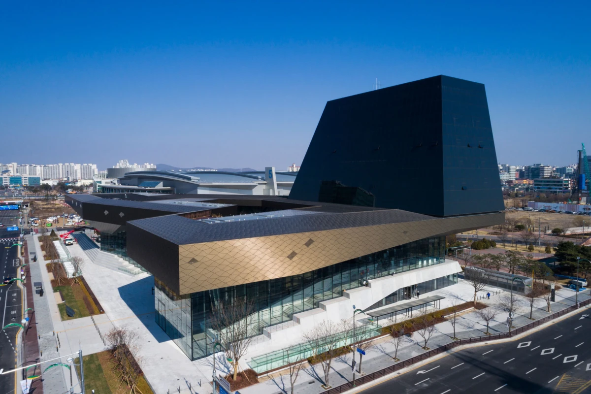 Modern cultural center with gold angular facade and a tall black prism, in an urban cityscape.