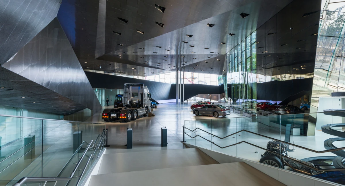Large semi-truck on display with several cars inside a modern, angular automotive showroom.