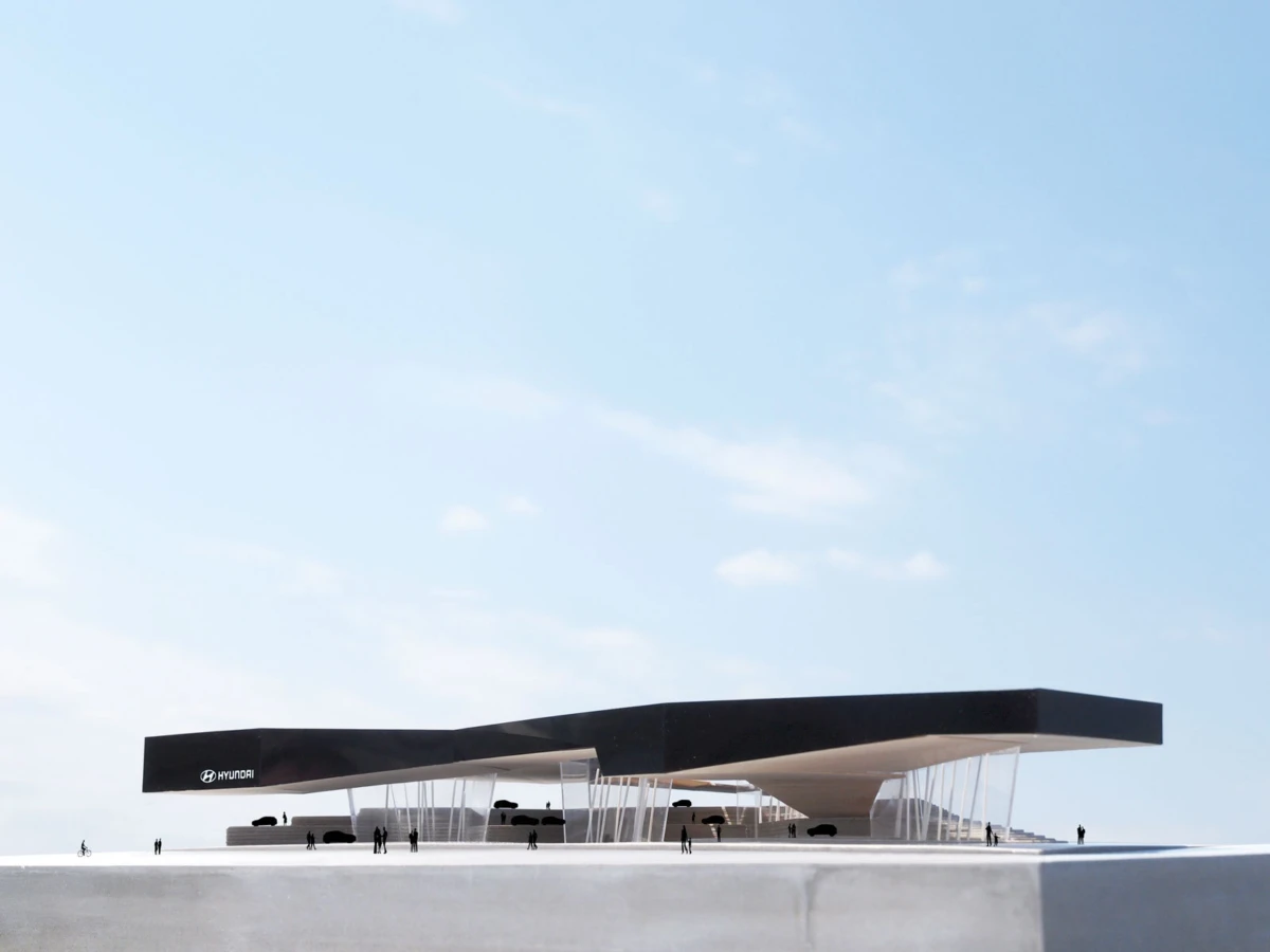 Contemporary pavilion with a long black cantilevered roof atop white columns, silhouettes of people nearby, blue sky.