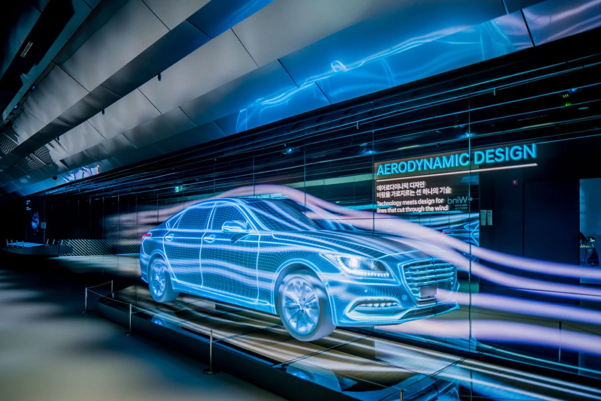 Blue holographic wireframe car displayed in a futuristic showroom; background signage reads AERODYNAMIC DESIGN.