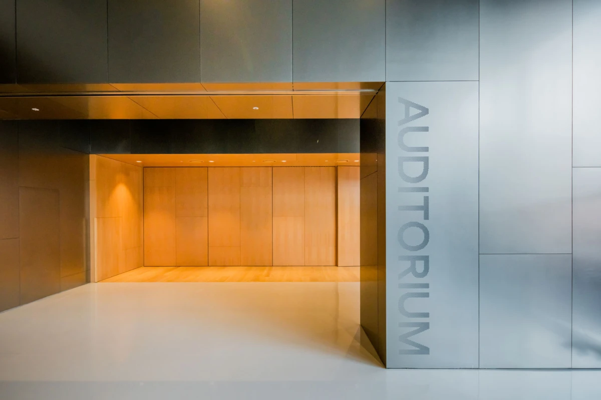 Open doorway into a wood-paneled auditorium interior; metal walls frame the entrance, with the word AUDITORIUM on the right.