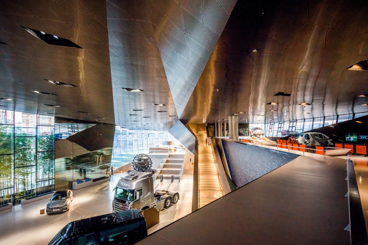 Futuristic automotive showroom interior with a silver semi-truck and several cars on display among glass walls and metal architecture.