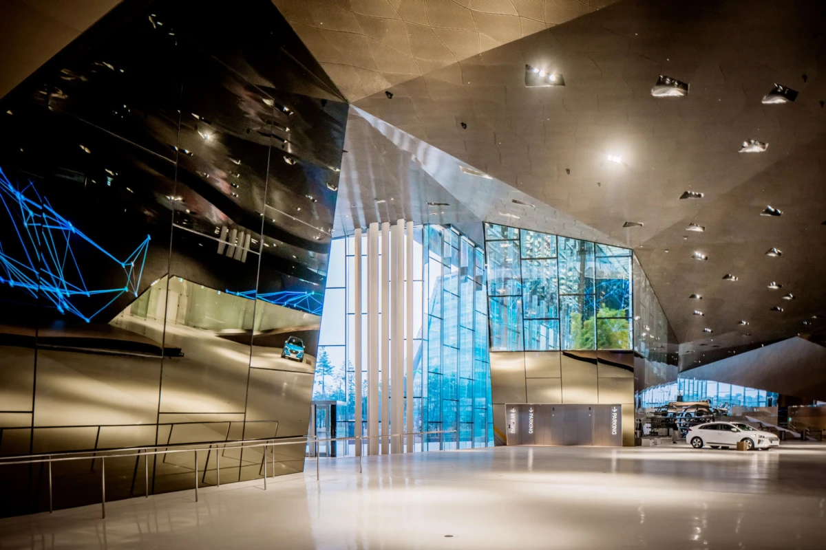 Futuristic car showroom interior with reflective black walls, blue light lines, and several cars near a glass entrance.