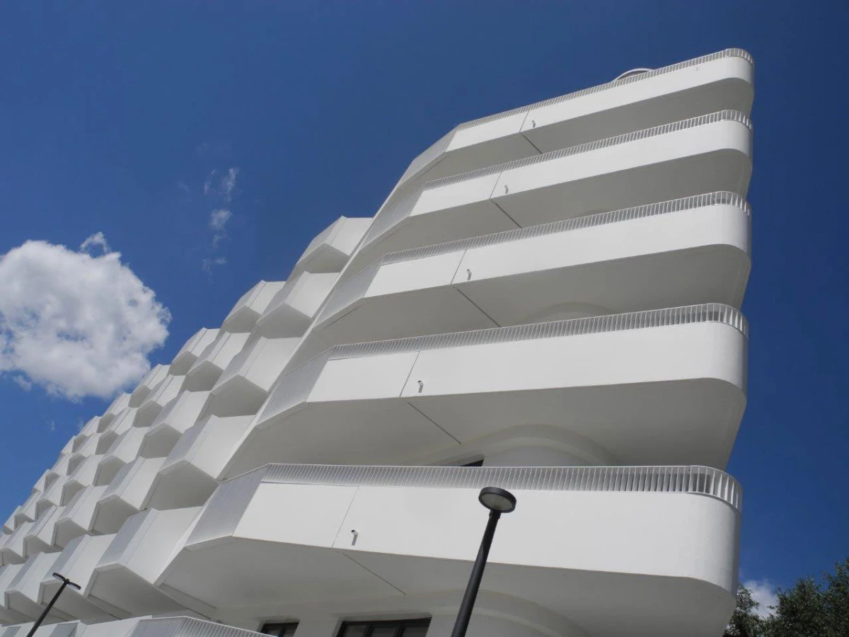 White modern apartment building with stacked curved balconies against a blue sky; street lamp in the foreground.
