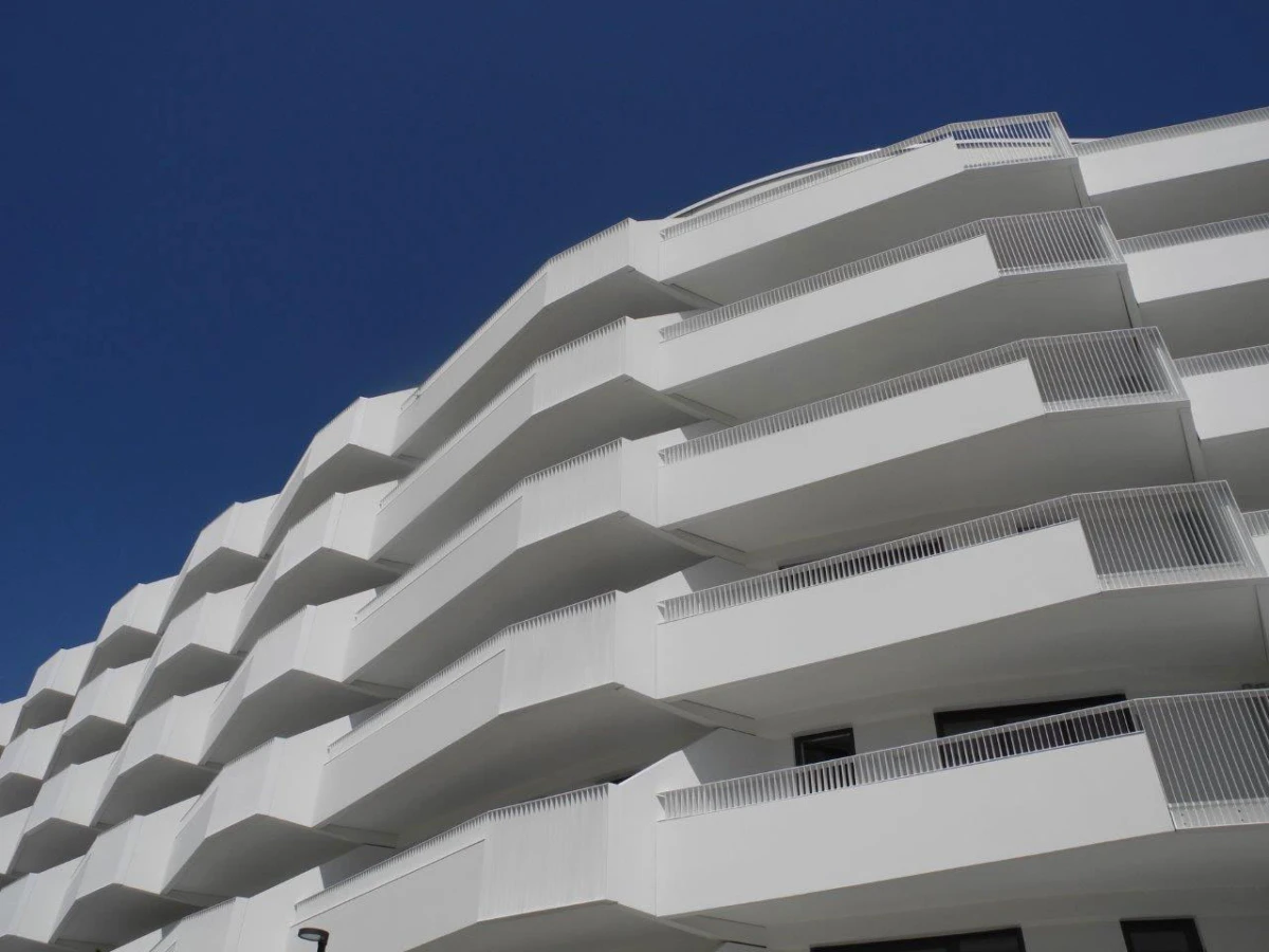 White apartment building with stacked balconies against a blue sky.