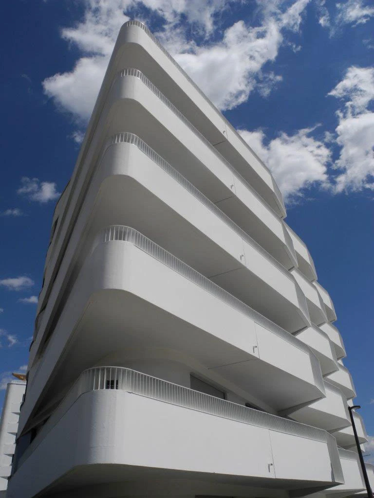 White modern apartment building with stacked curved balconies against a blue sky.