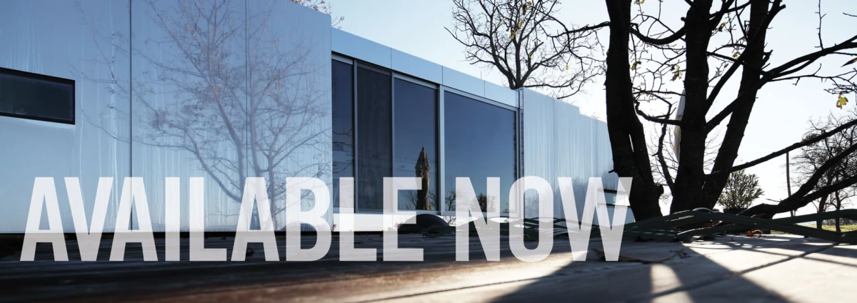 Modern glass-front building exterior; tree shadows on ground; prominent overlay text AVAILABLE NOW