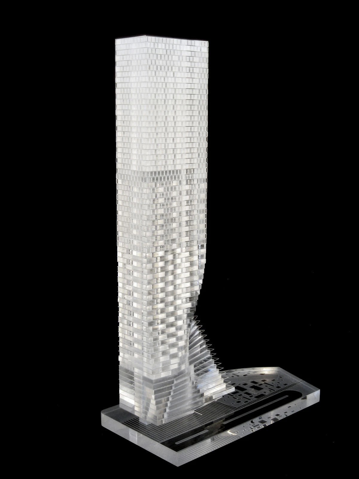 Transparent glass-block skyscraper model standing on a rectangular display stand against a black background.
