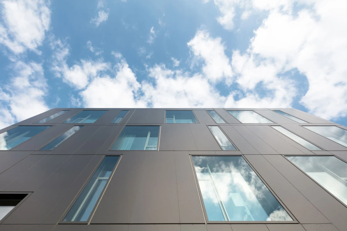 Low-angle view of a grey panelled building facade with rectangular windows against a blue sky.