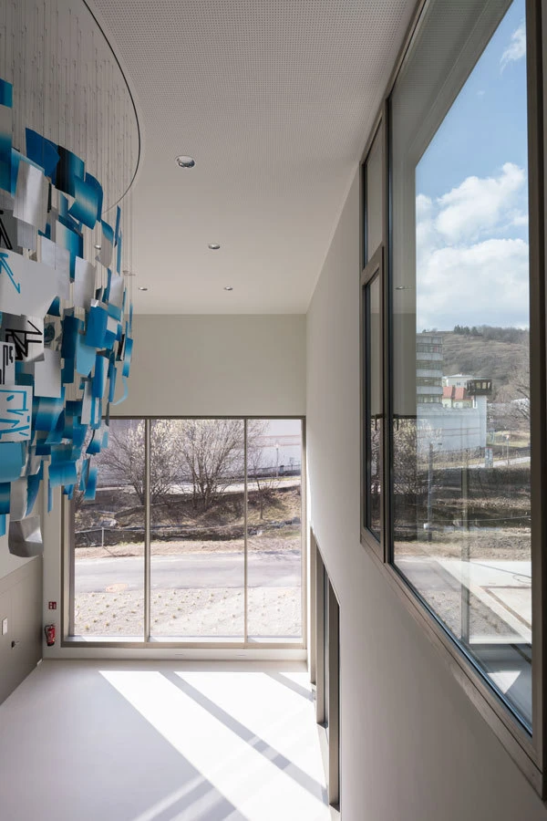 Curved white wall installation of blue and white hanging cards in a bright atrium with large windows and an outdoor view.