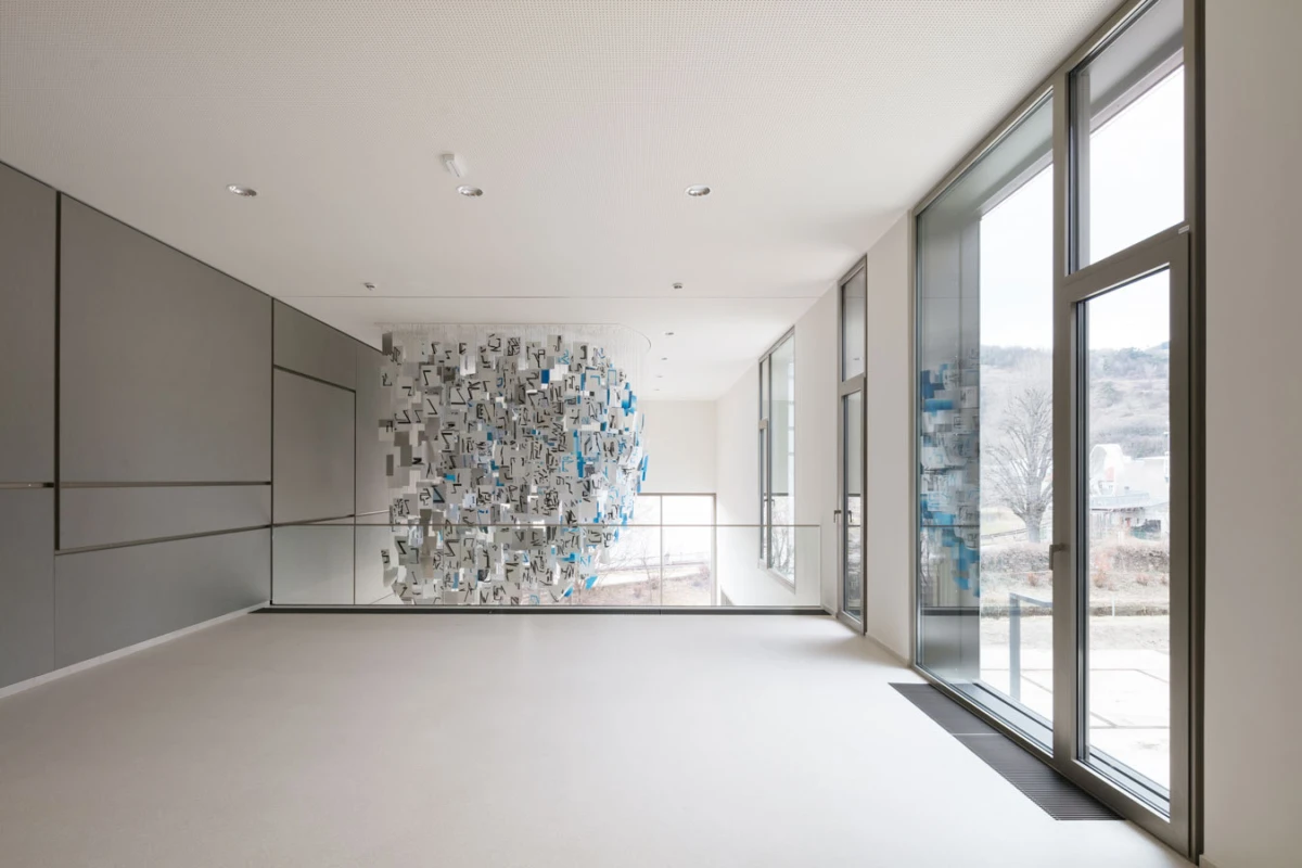 Suspended sphere-shaped installation of hanging cards in a modern hallway with floor-to-ceiling windows.