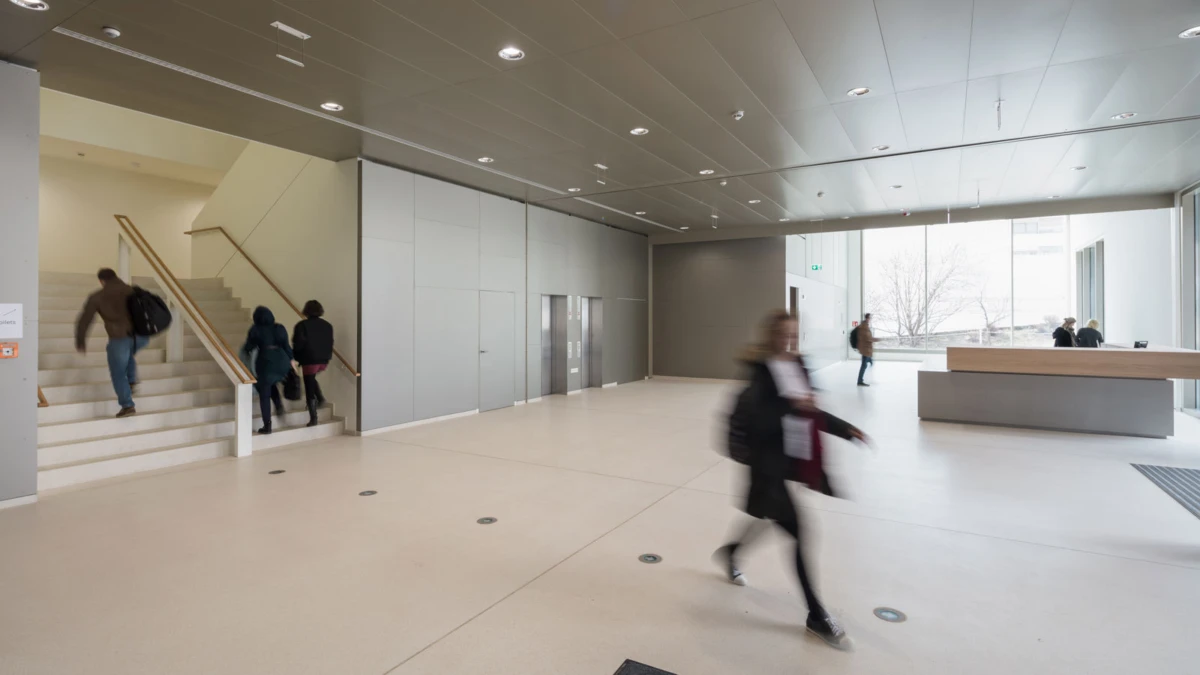 Blurred person walking through a spacious modern lobby; reception desk on the right and a staircase on the left.