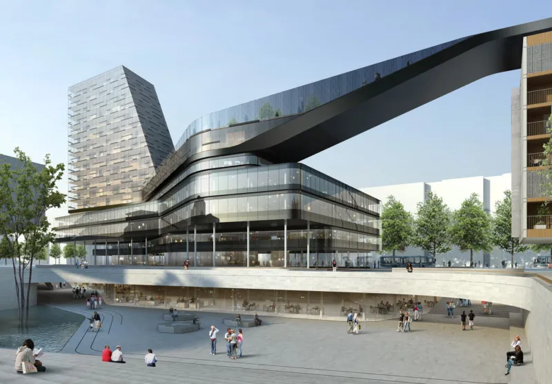 Futuristic glass-fronted building with a curved skybridge over a pedestrian plaza; trees, a water feature, and people walking and sitting.