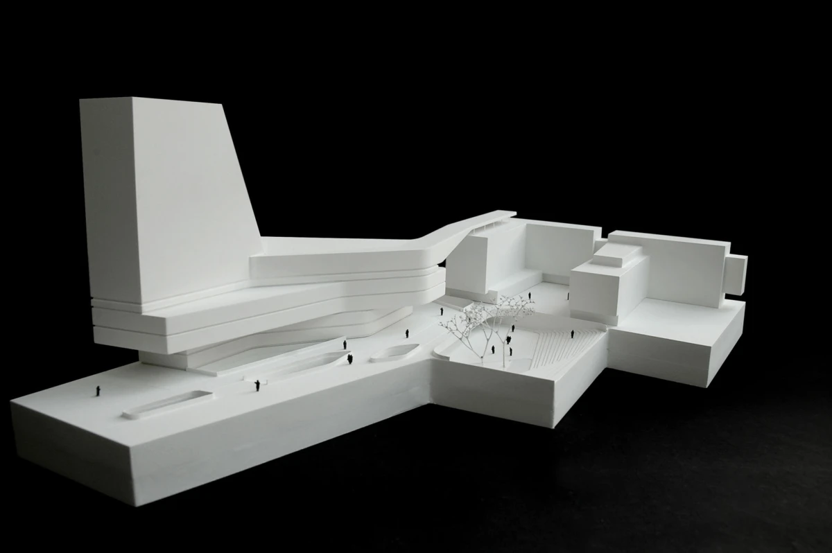 White architectural model of a modern multi-level building with terraces and a plaza, tiny trees and people, on a black background.