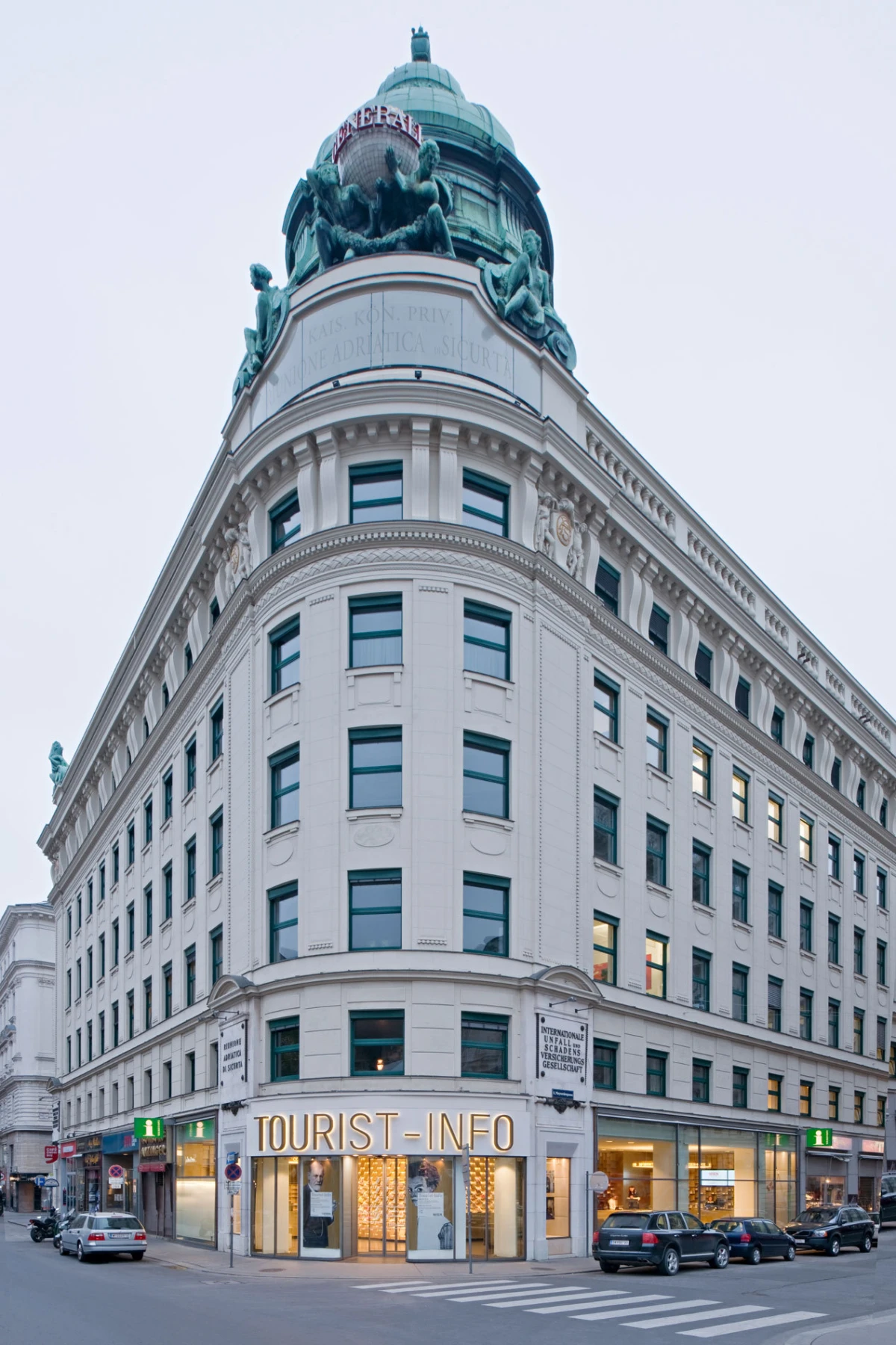 Corner white historic building with a copper-domed top and sculpted statues; ground-floor TOURIST-INFO storefront.