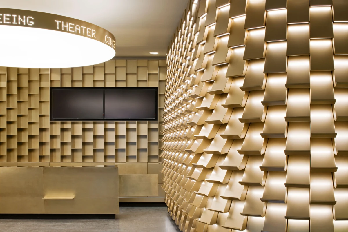 Beige 3D acoustic-panel wall in a modern lobby; circular ceiling sign, wall-mounted screen, and beige benches.