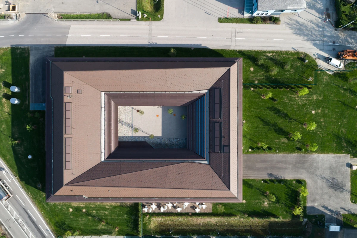 Aerial view of a square brown-roofed building with a central open courtyard, bordered by green lawns and roads.