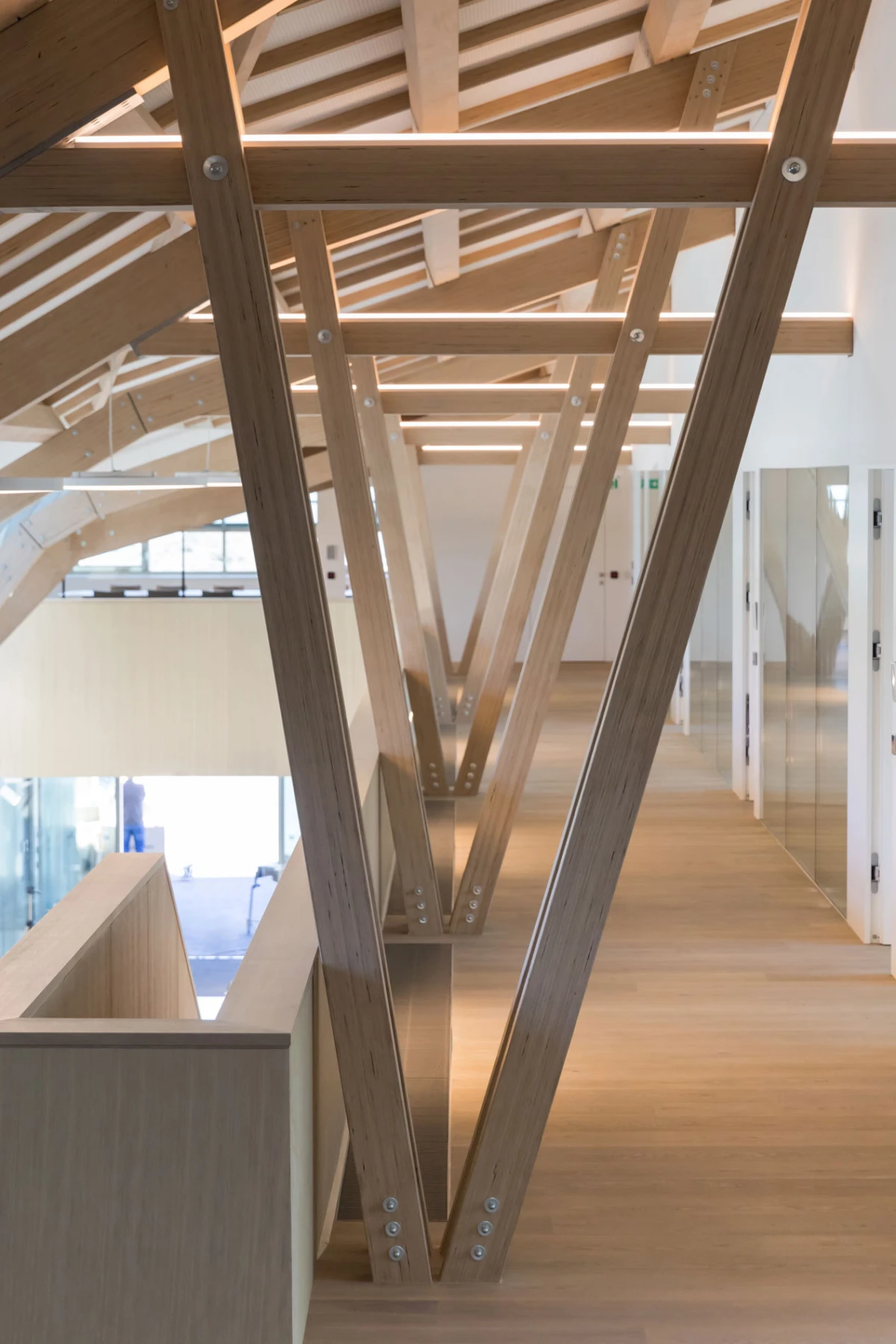 Interior corridor with large V-shaped wooden trusses forming the ceiling framework.