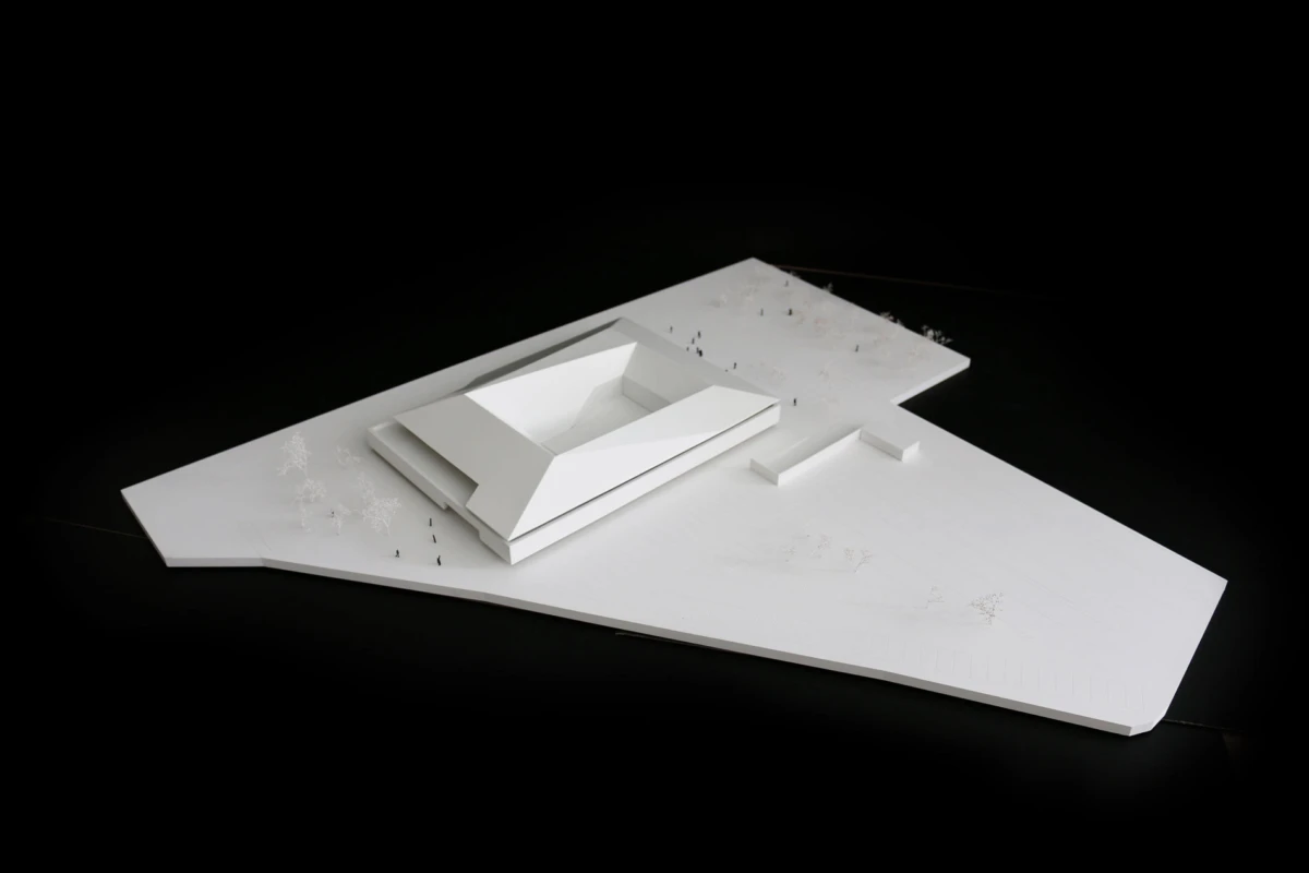 White architectural model of a multi-tiered, angular building on a white platform with scale figures, set against a black background.