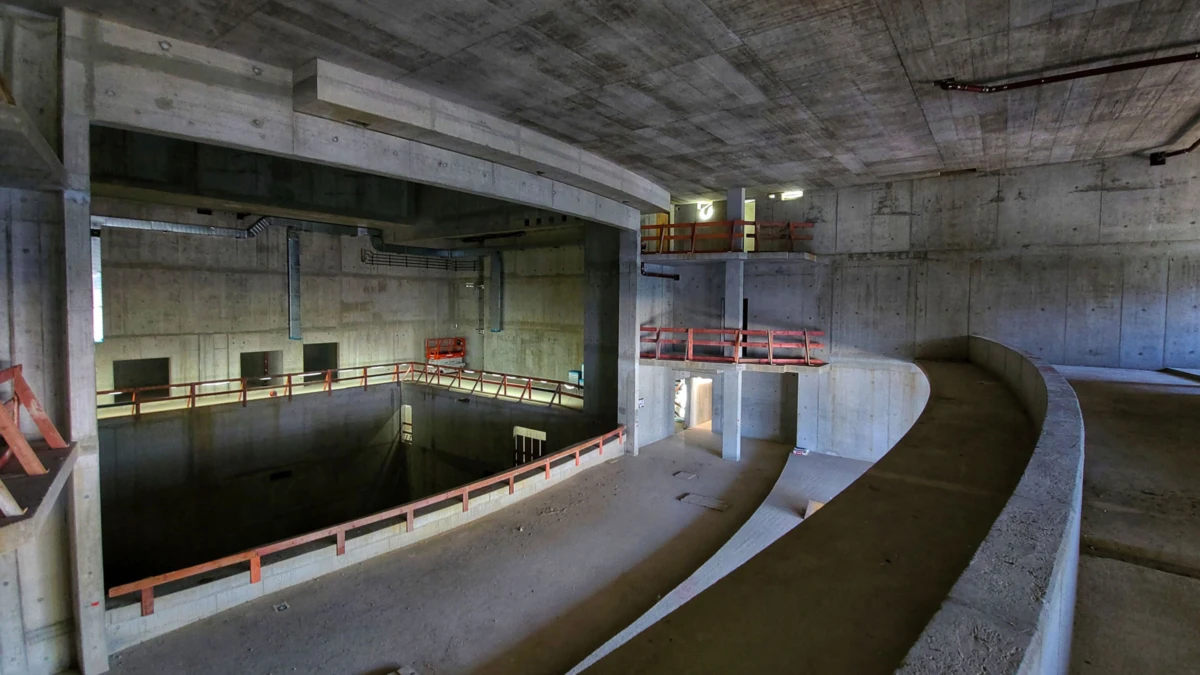 Partially finished concrete construction site with a curved ramp circling a deep open pit, red guard rails, and elevated platforms.