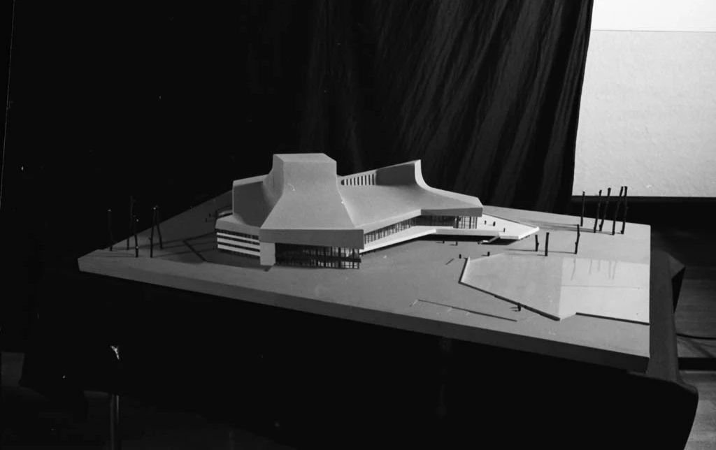 Scale model of a contemporary building with sweeping curved roofs on a display base.