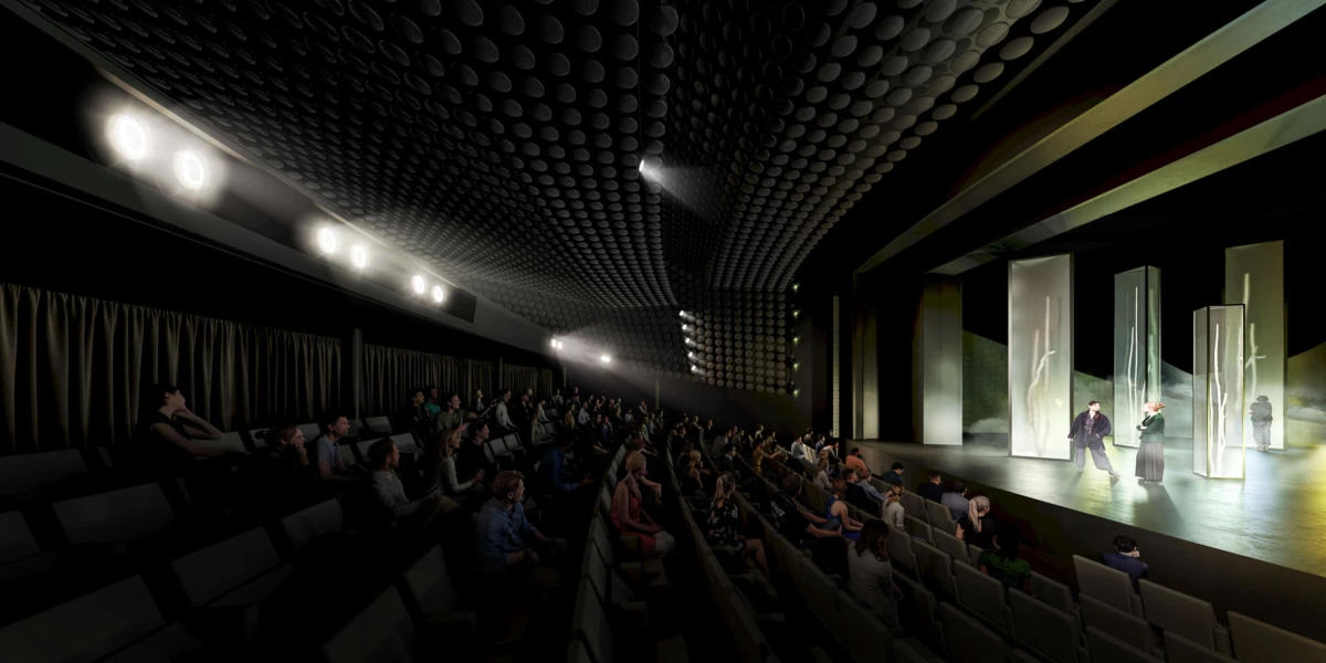 Dim theater auditorium; two performers on a lit stage beside tall translucent panels, as an audience watches.