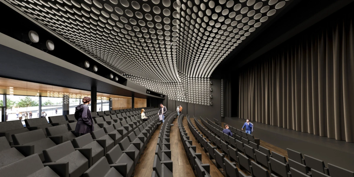 Interior of a modern auditorium with curved gray seating; people walk along aisles toward the stage; perforated ceiling panels and dark curtains.