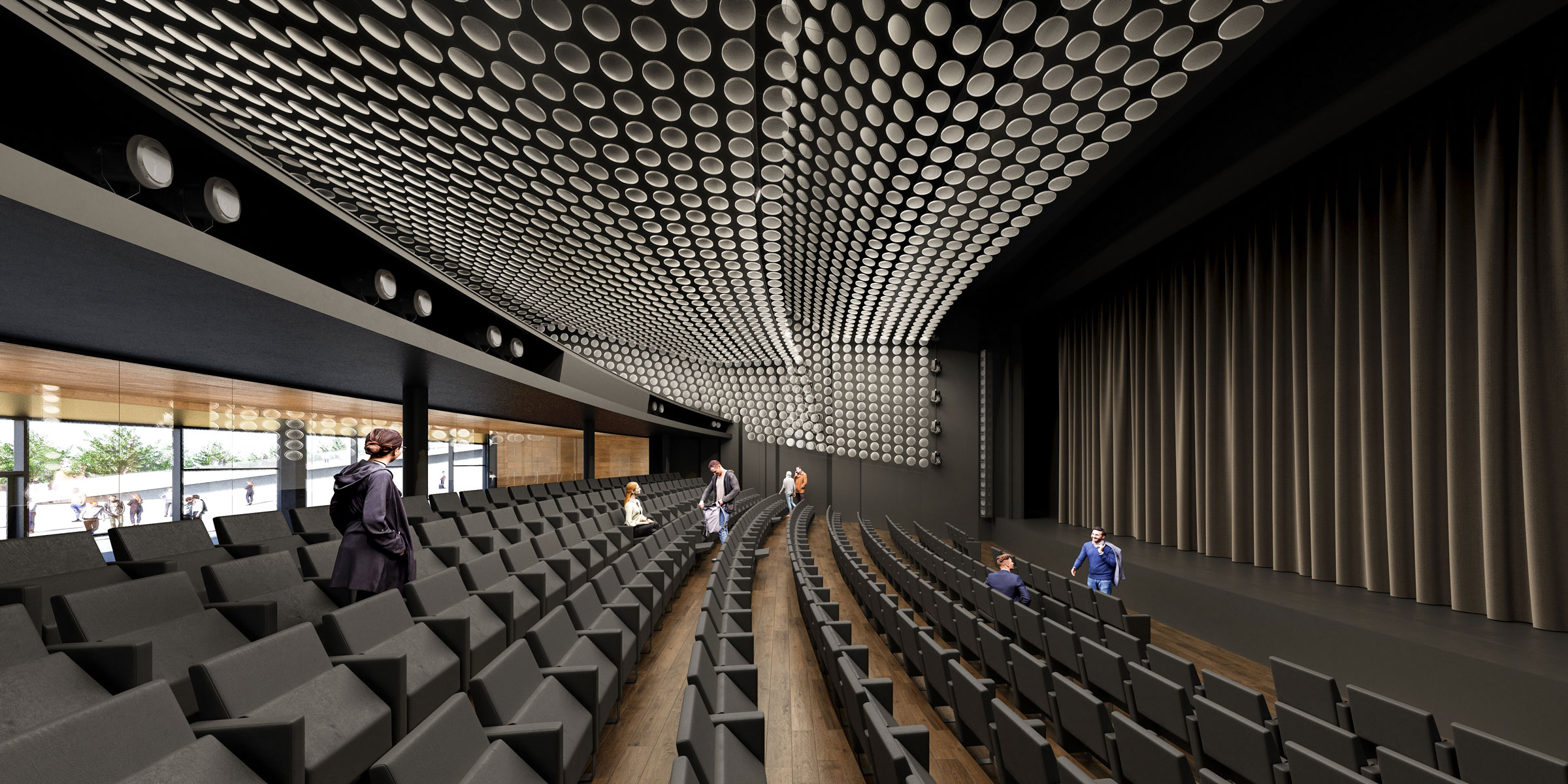 Modern theater interior with curved rows of dark seats and a stage with closed curtains; a few people walk in the aisles.
