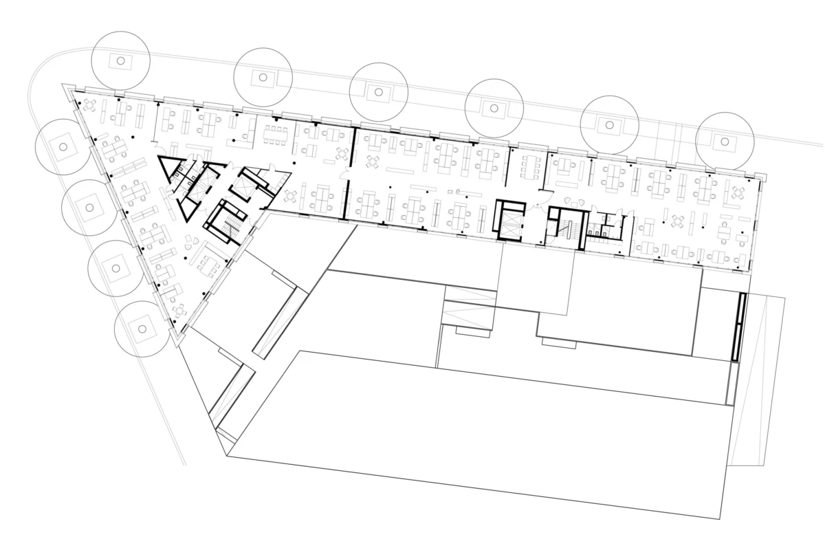 Architectural floor plan of an office building: long corridor with rows of desks, triangular wing with meeting rooms, and circular site elements.