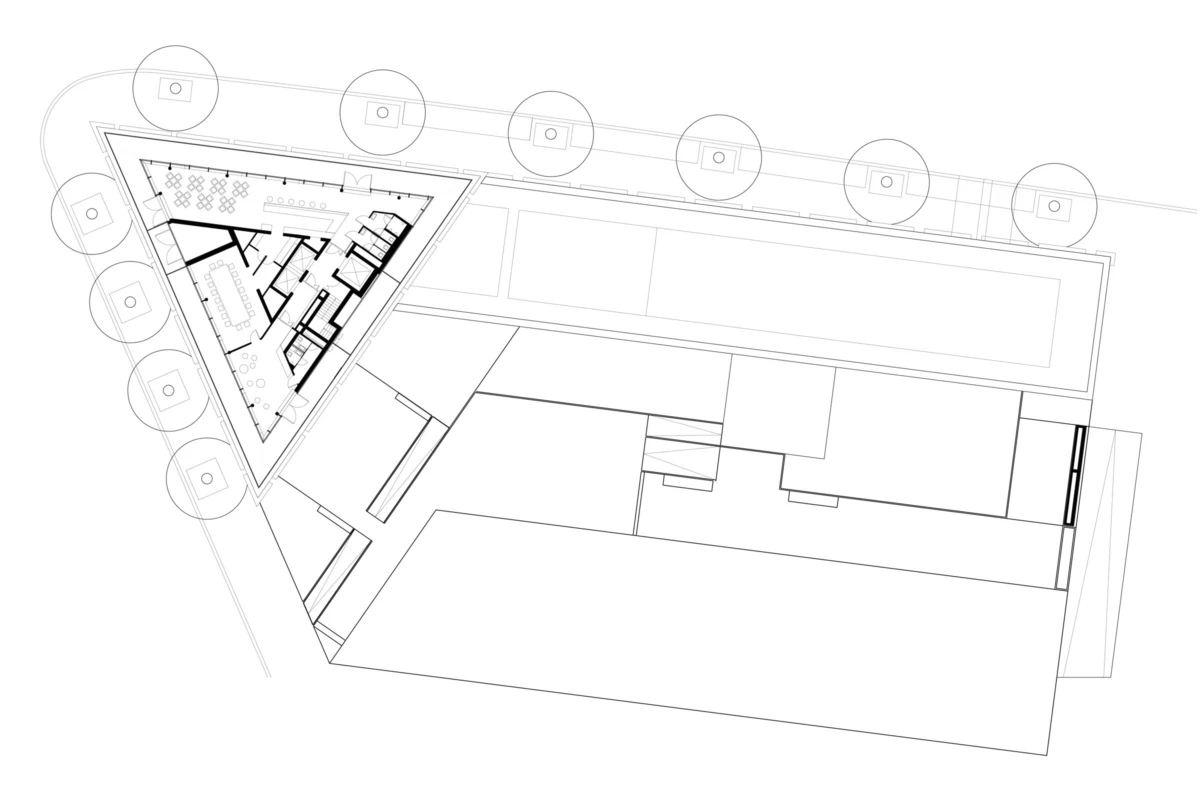 Architectural floor plan: triangular-wing building with interior rooms beside a rectangular block; circular trees line the outer boundary.