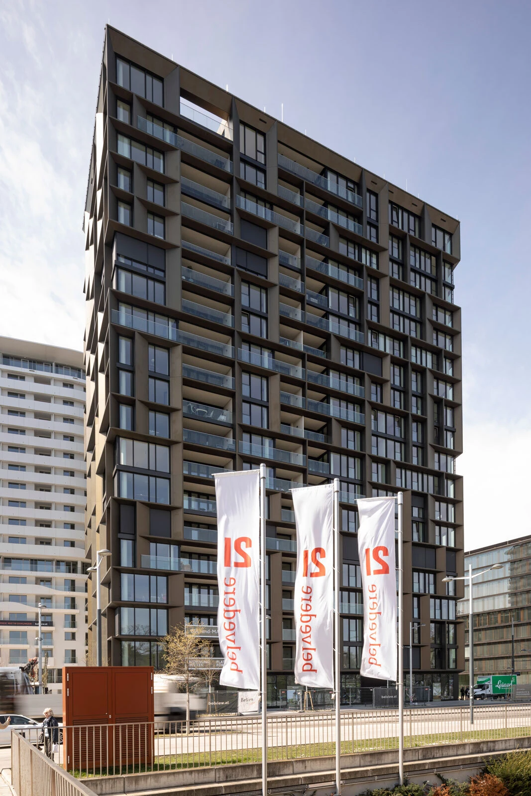 Tall modern residential tower with glass balconies; three white flags bearing red IS logos in the foreground.