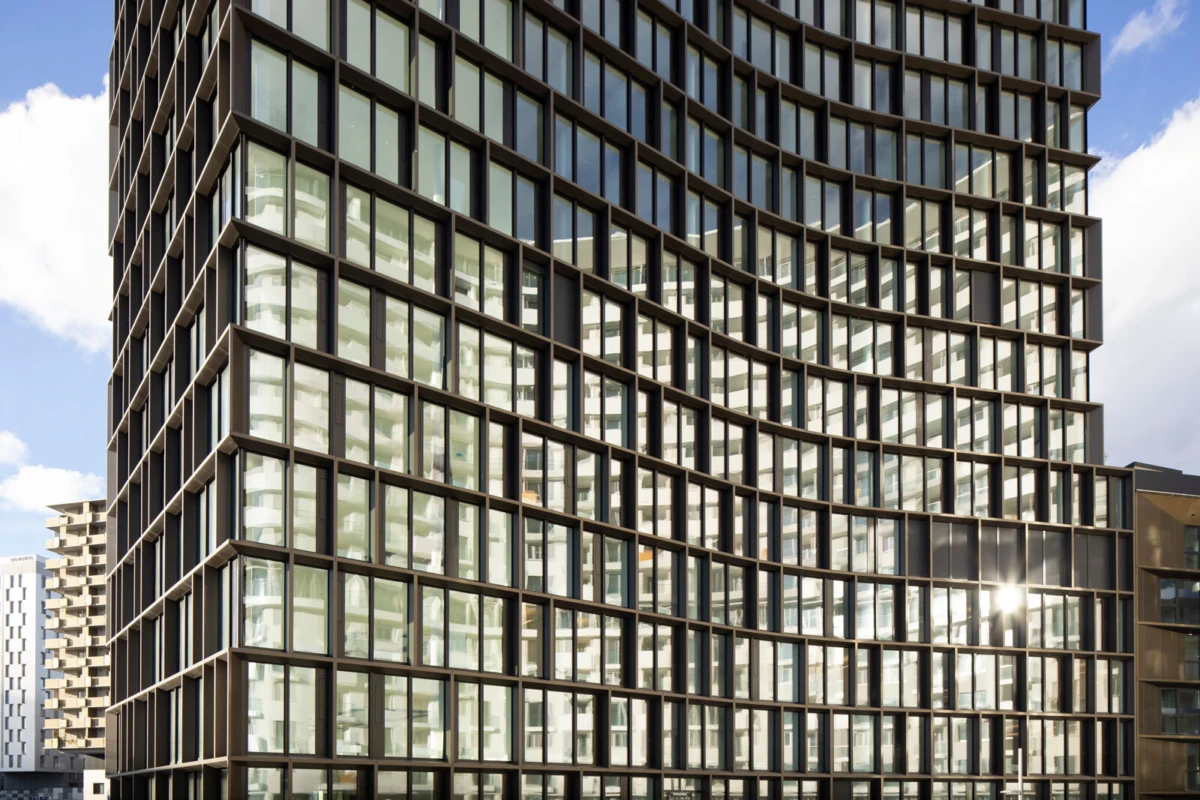 Glass-clad high-rise with a grid of square windows; sunlight glints off reflective panes in an urban daytime setting.