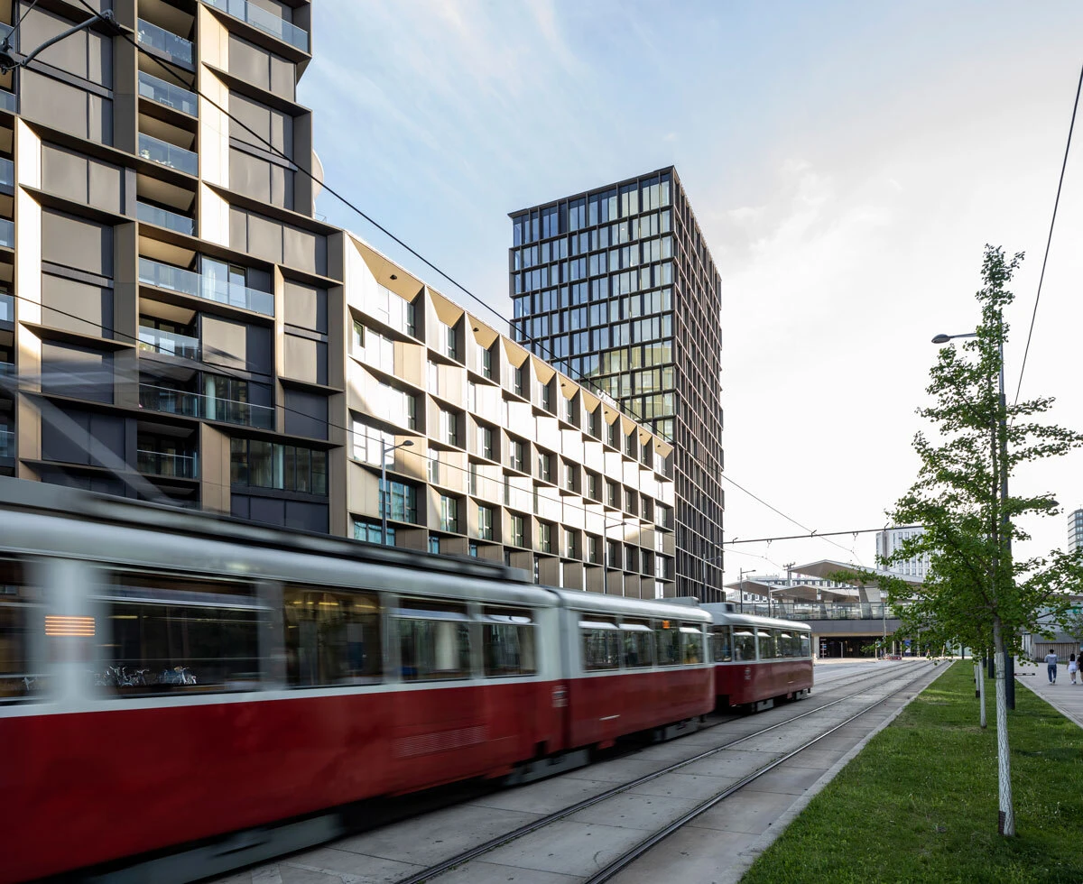Red tram travels along tracks beside modern apartment buildings in an urban cityscape.
