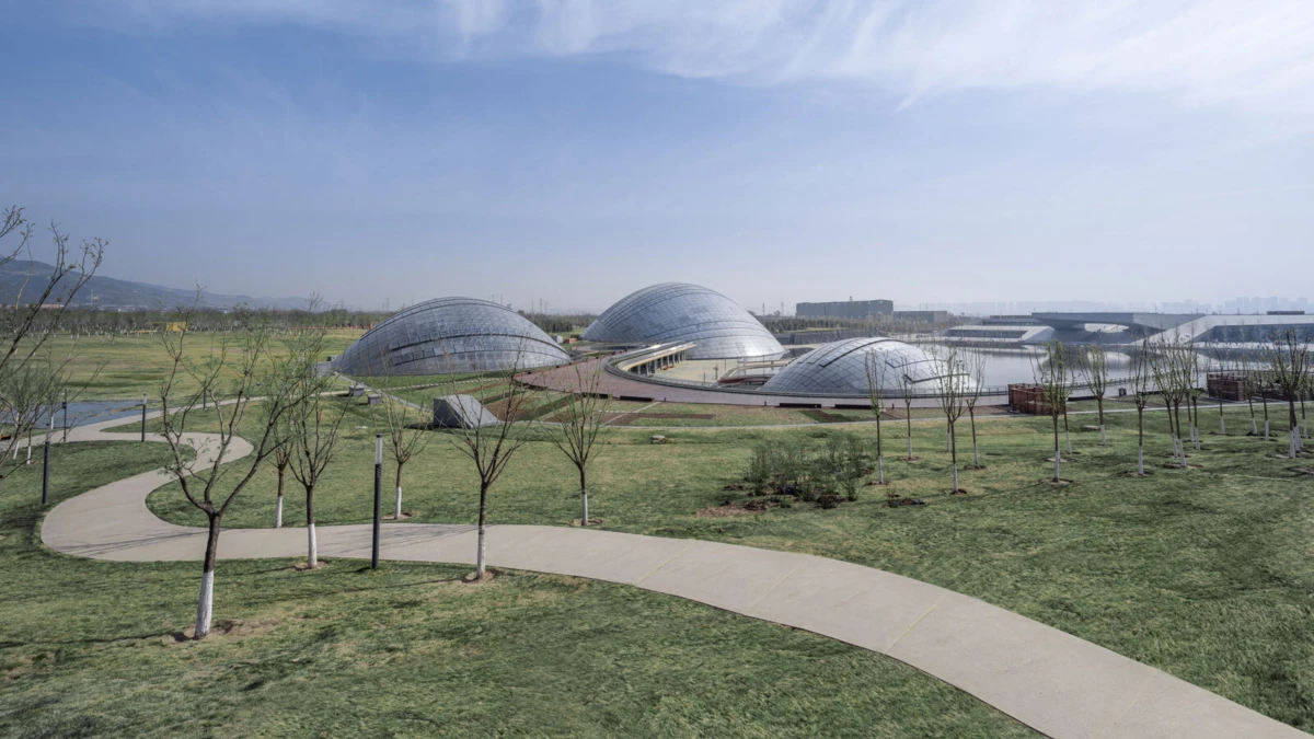 Glass geodesic domes in a landscaped park with curved walkway, leafless trees, and a tranquil water feature.