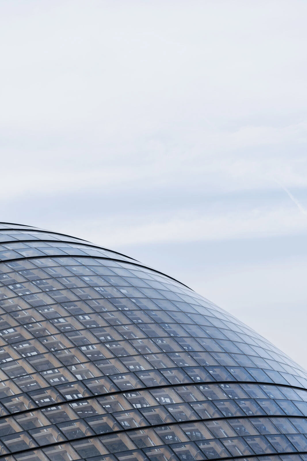 Curved glass-dome building with a grid of panes, set against a pale blue sky.